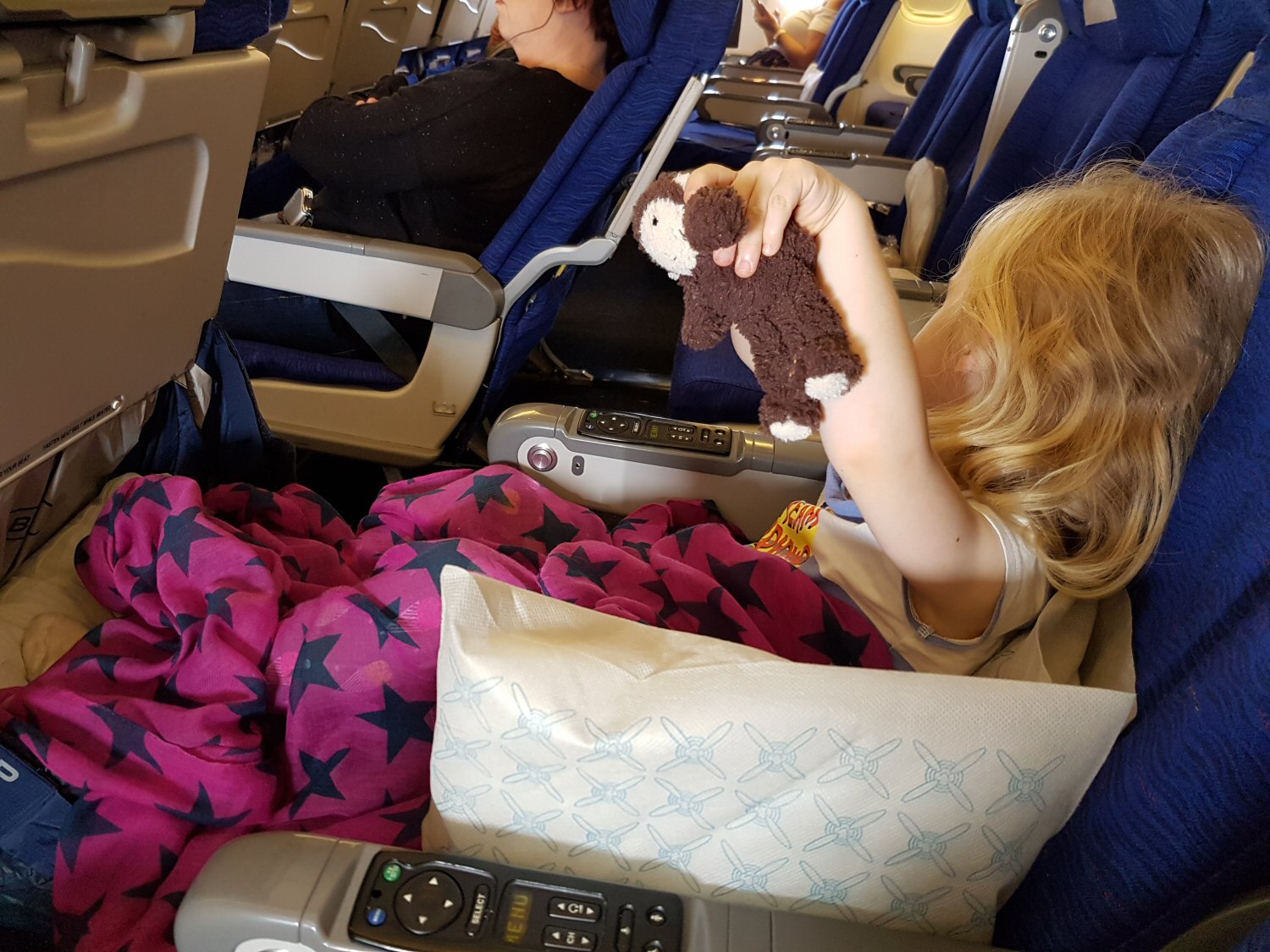 My daughter holds her toy monkey in her plane seat, her legs up on her Kids Fly Legs up flight hammock