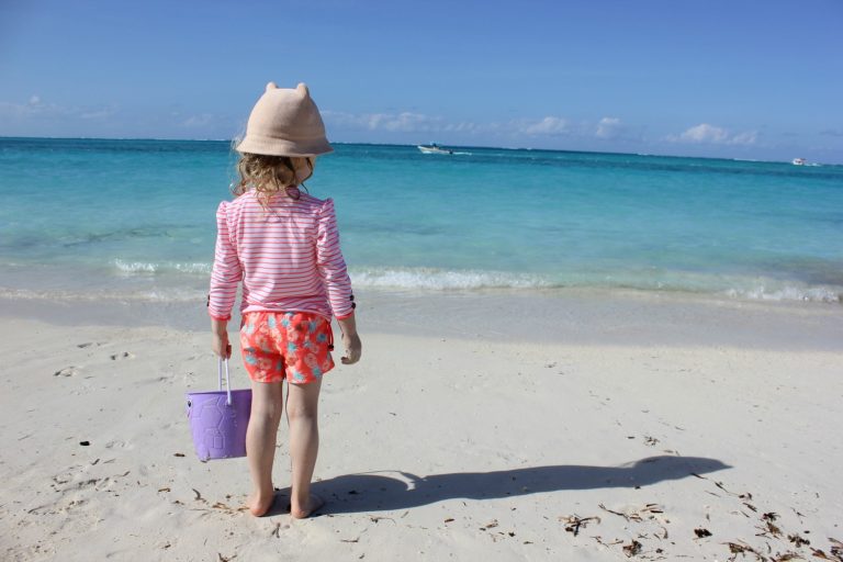 A girl on a beach holding a bucket looks out onto the Caribbean sea - my Sunuva girls swimwear review