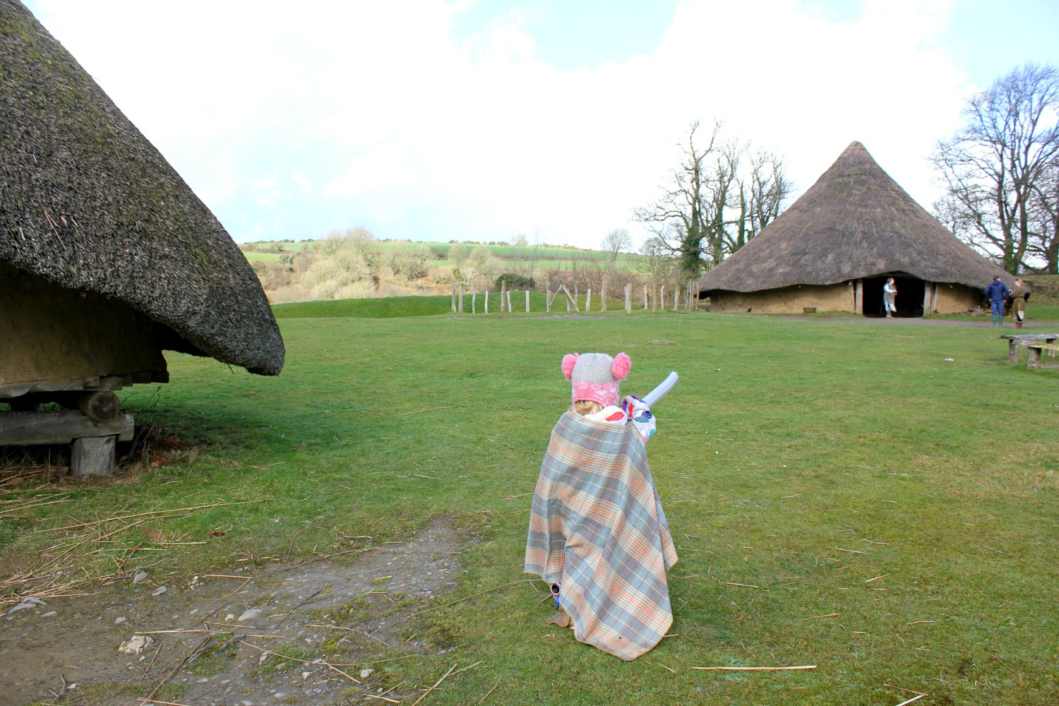 Girl in Celtic cloak walks past roundhouses at Castell Henllys Iron Age village in Wales - one of my three top days out in Pembrokeshire with kids
