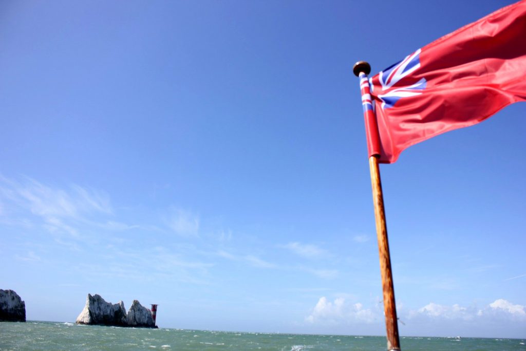 A flag flying in the breeze with The Needles behind - discovering the Isle of Wight coast