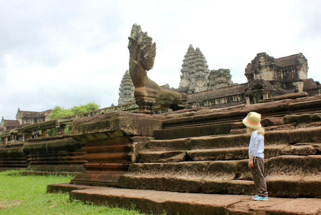 My daughter stands by weathered stone steps and looks up towards the stone carvings around Angkor Wat during a trip to Cambodia with kids