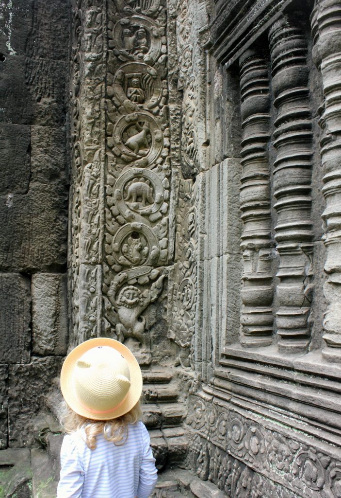 My daughter looks at the unusual animal carving at Ta Prohm in Cambodia which resembles a stegosaurus - visiting the temples of Angkor with kids