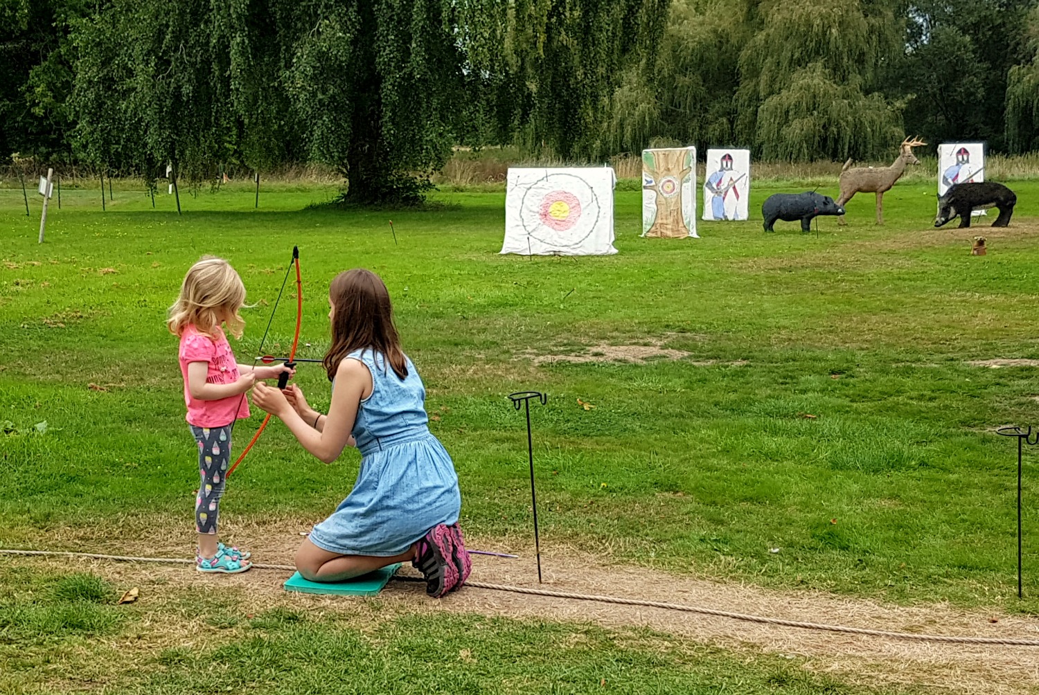 My daughter stands in front of targets to practise her archery skills assisted by a helper at Hever Castle, Kent