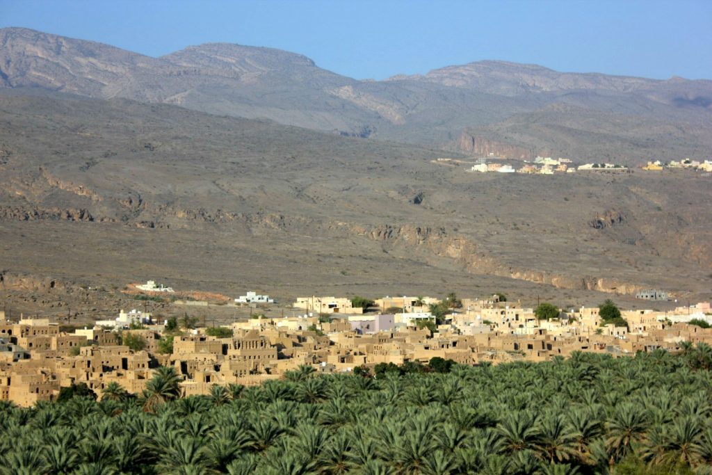 A view of the lush green date palms and a village in the wadi in the shadow of the Hajar Mountains in Oman - my nine reasons to visit Oman with kids