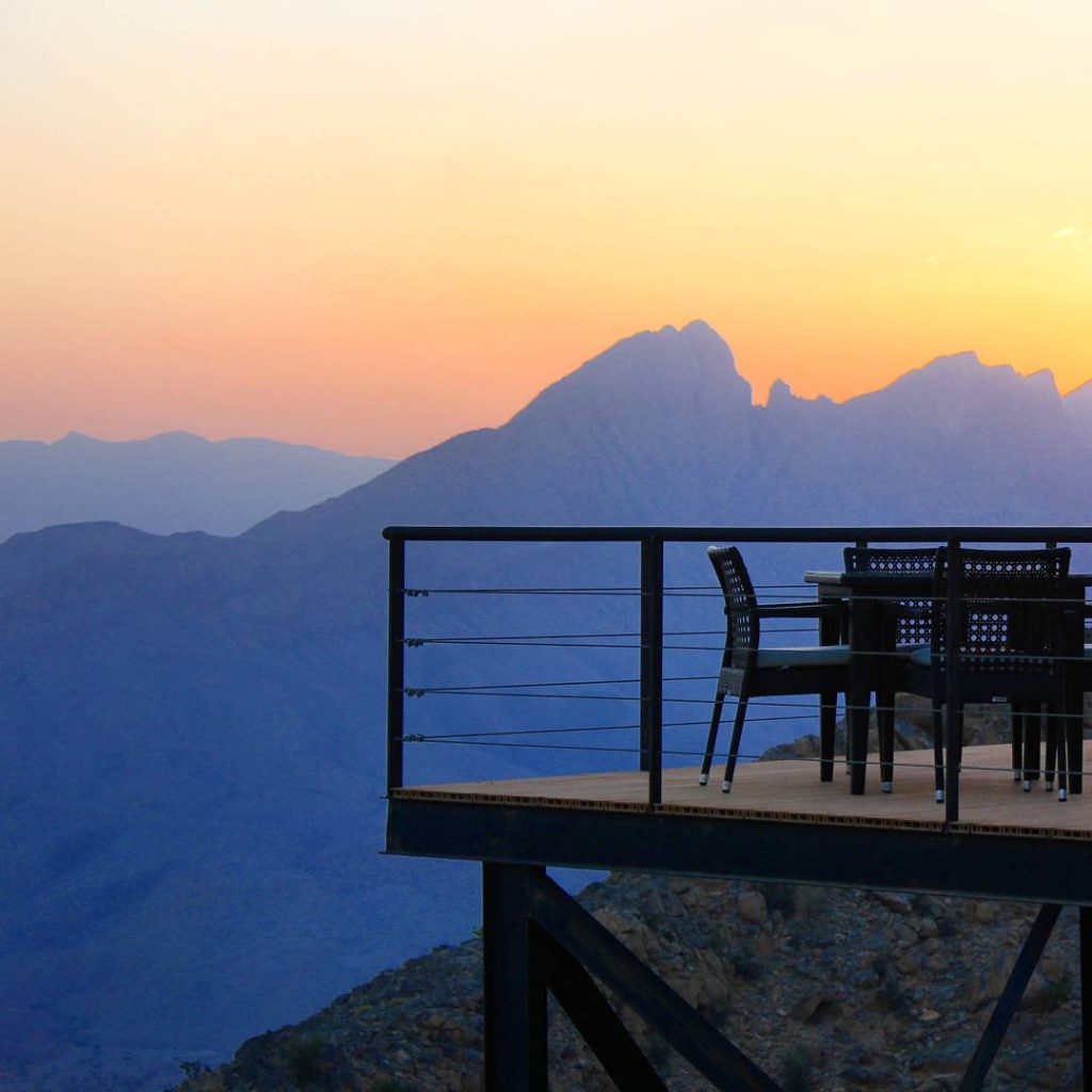 A sunset view out to the Hajar Mountains from The View Hotel in Oman, with the edge of the restaurant terrace on stilts visible with the peaks behind - my nine reasons to visit Oman with kids