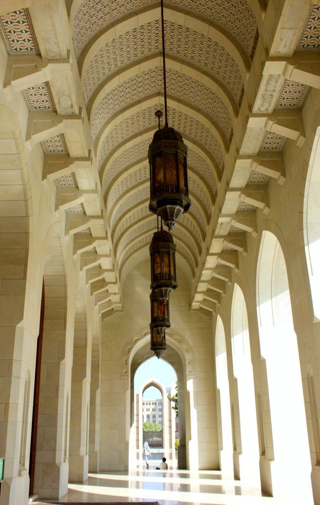 Light streams through archways along a covered walkway to another arch in the Sultan Qaboos Grand Mosque in Muscat Oman - the beautiful architecture is one of my nine reasons to visit Oman with kids