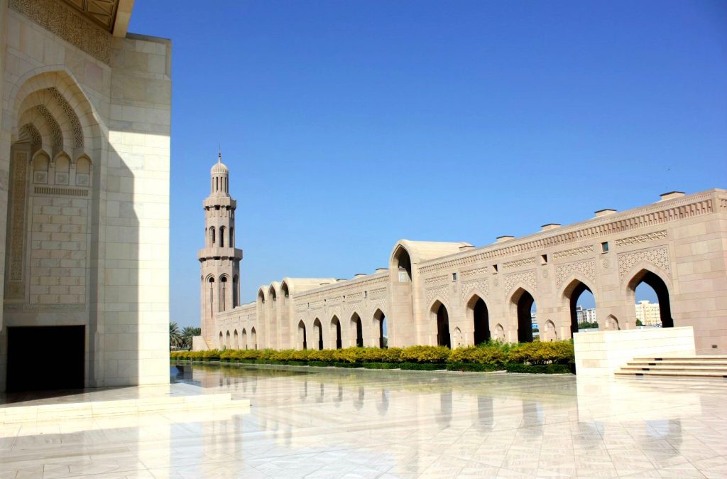 A view of a gleaming courtyard, minaret and buildings of the Sultan Qaboos Grand Mosque in Muscat Oman - the beautiful architecture is one of my nine reasons to visit Oman with kids
