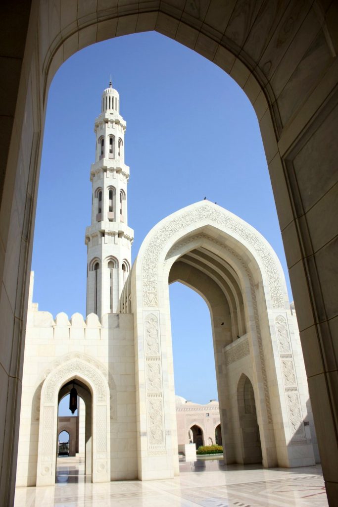 A view of one of the ornate white minarets above an archway at the Sultan Qaboos Grand Mosque in Muscat Oman - the beautiful architecture is one of my nine reasons to visit Oman with kids