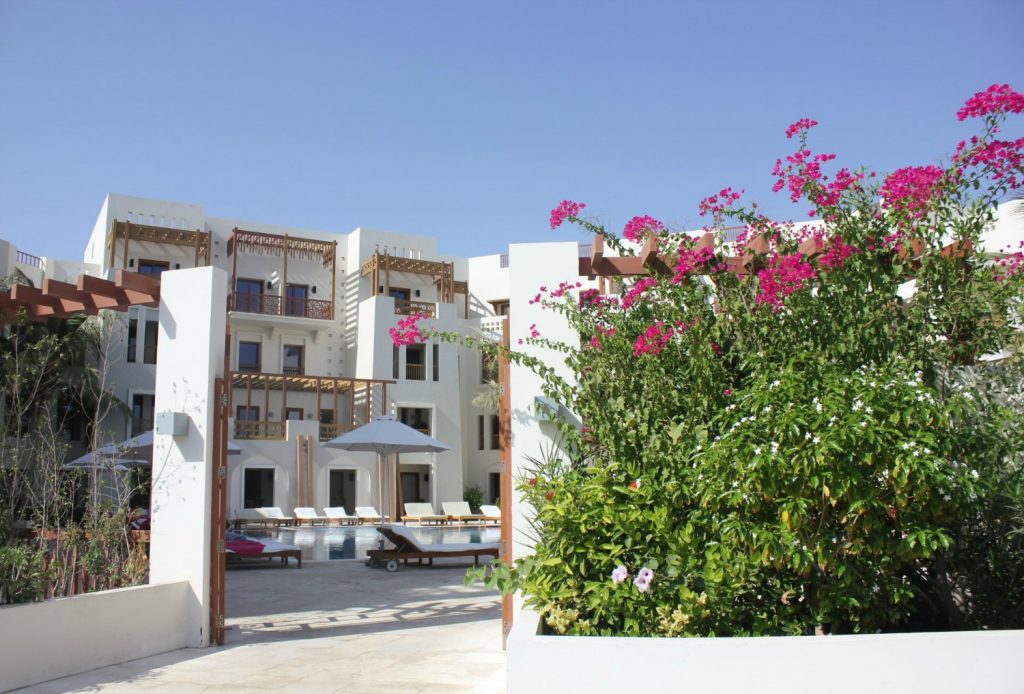 The white buildings of Sifawy Boutique Hotel seen through a gate with pink bougainvillea not far from Muscat, Oman - my nine reasons to visit Oman with kids