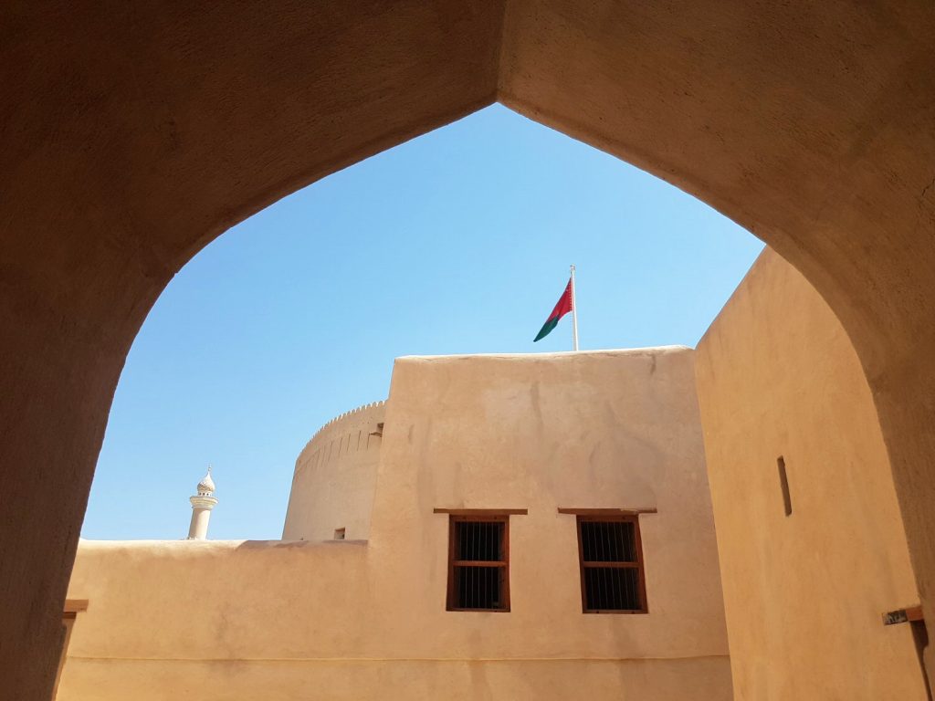 A view of a flag flying above the buildings of Nizwa fort in Oman seen through a pointed archway - my nine reasons to visit Oman with kids