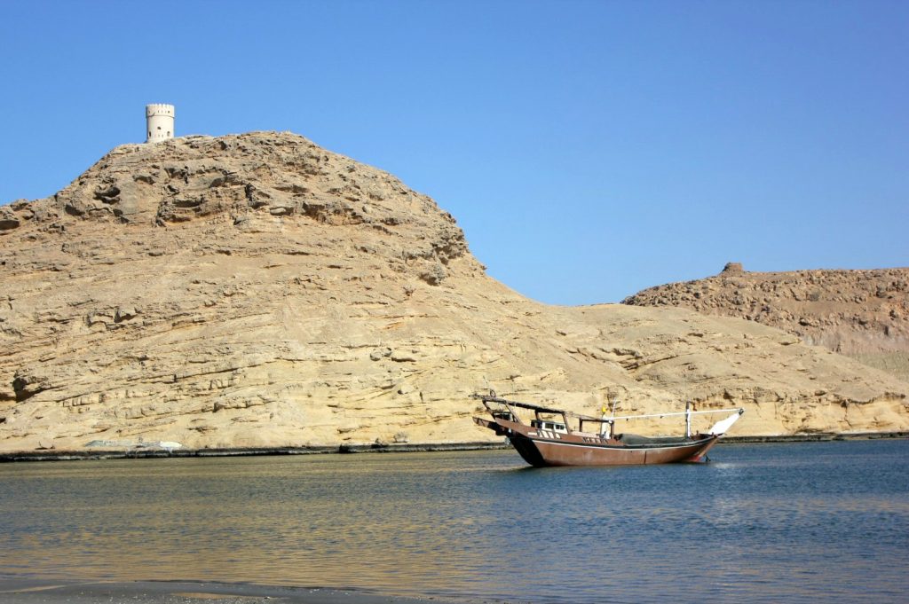 A wooden dhow boat in the water with a rock cliff behind at Sur in Oman - my nine reasons to visit Oman with kids