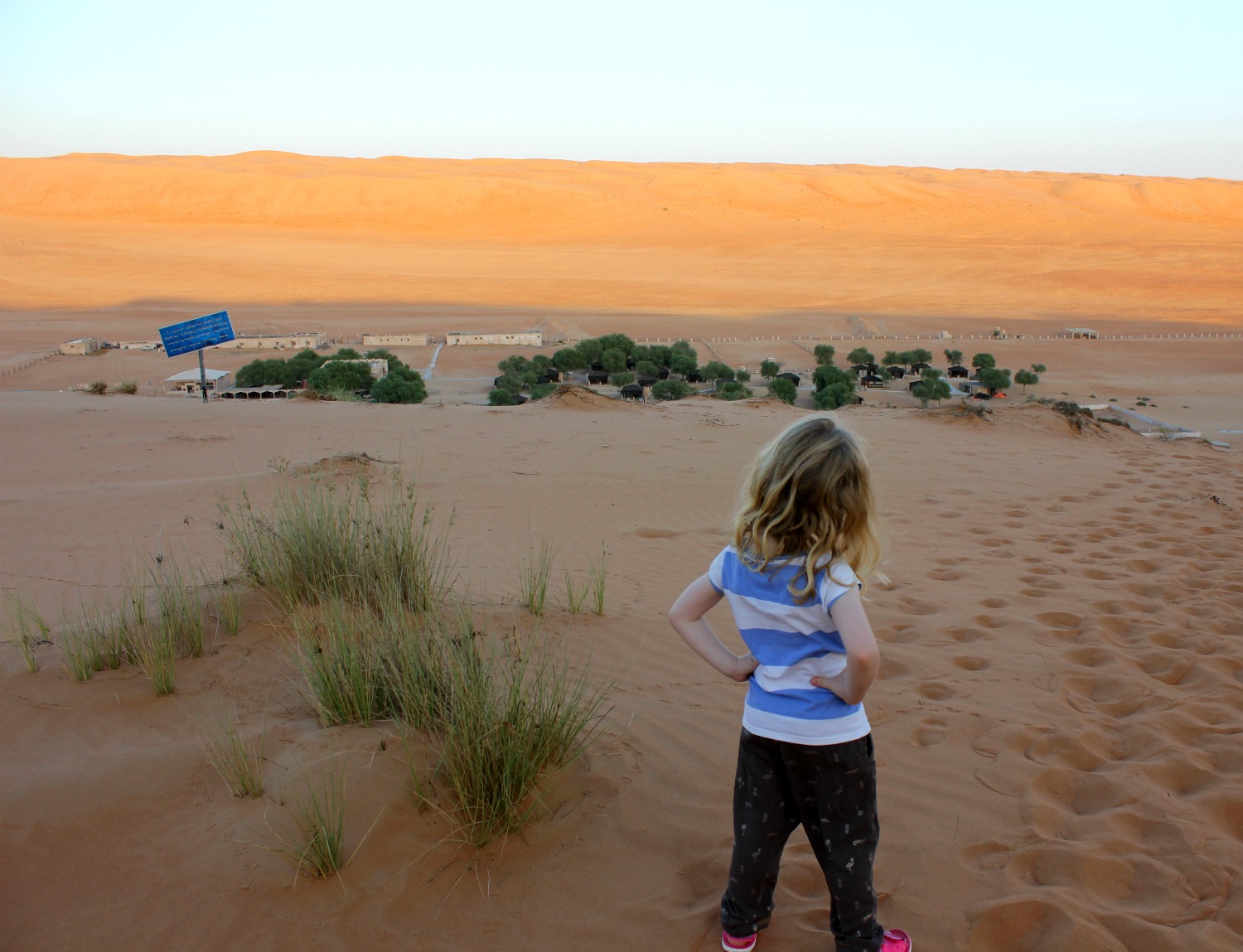 My daughter looking down from a sand dune onto a desert camp - my itinerary for a week in Oman with kids