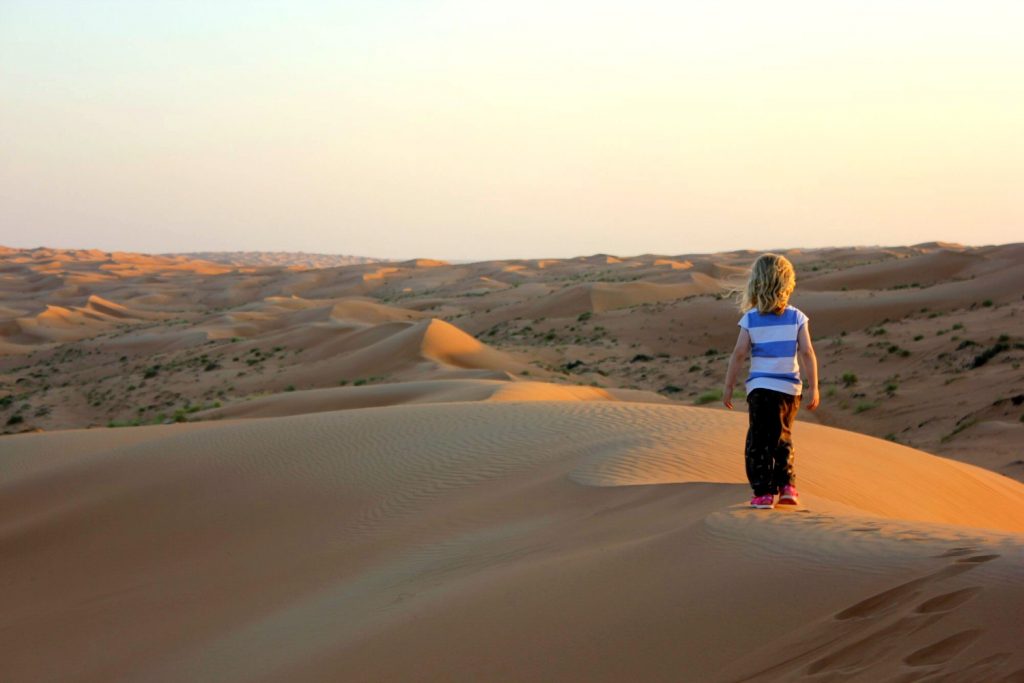 My daughter watches the sun set over the orange dunes stretching into the distance at Wahiba Sands in Oman - my nine reasons to visit Oman with kids
