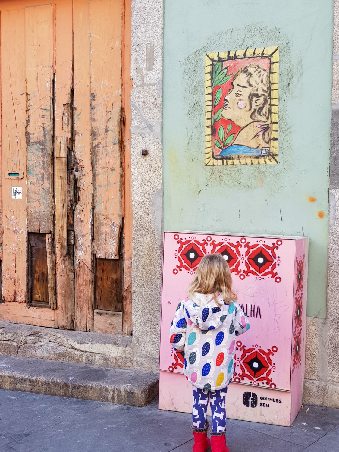 Girl looks at one of the painted electricity boxes on Rua das Flores in Porto, just some of the city's street art- a street art tour is one of the best things to do in Porto with teens