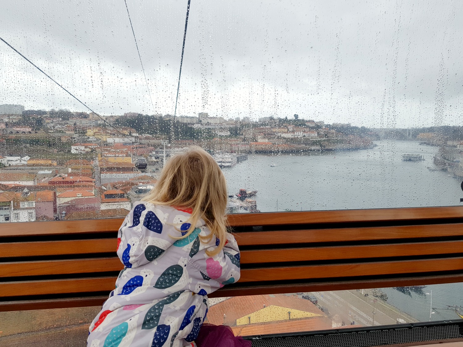 My daughter looks through the rainy window of the cable car to see the view across to the River Douro and Vila Nova de Gaia - one of the best things to do with kids in Porto, rain or shine