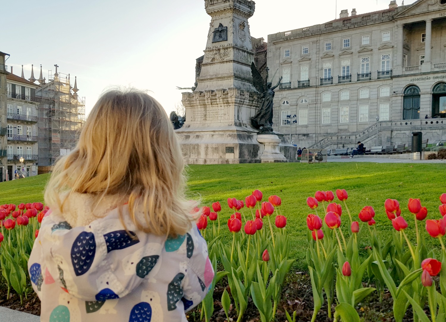 A girl looks across red tulips to a statue and square in Porto - my Porto travel tips and lessons for a city break there with kids