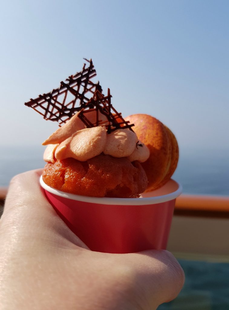A grand marnier cupcake and passion fruit macaron held up with the sea behind - the food is one of my 9 reasons families should choose Norwegian Bliss