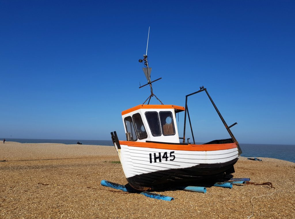A boat beached on the shingle at Aldeburgh against a bright blue sky - one of my things to do in Aldeburgh with kids if you're visiting Suffolk
