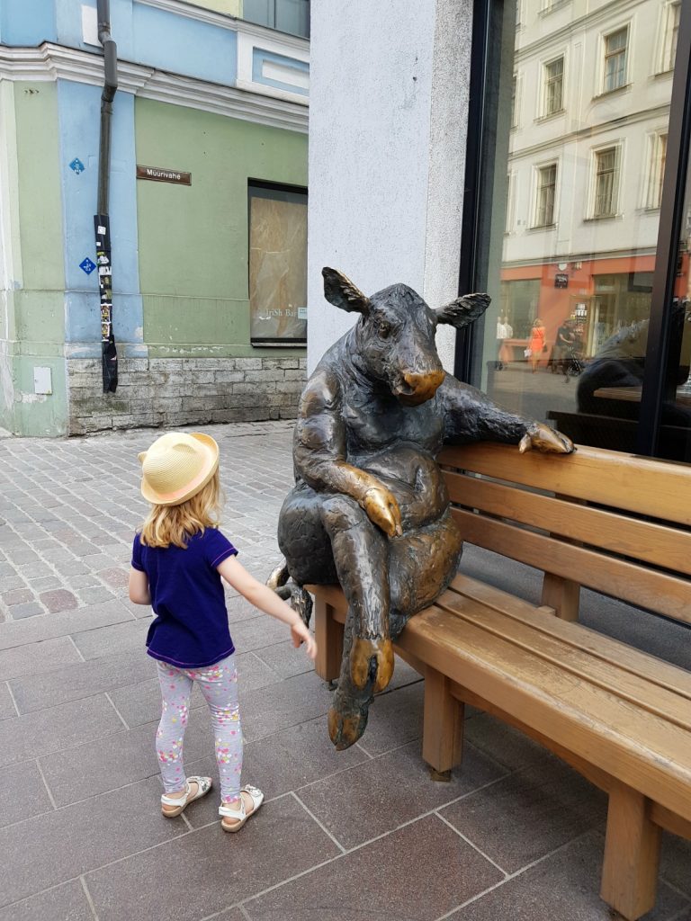 My daughter looks at a seated cow statue by a steak restaurant - the quirky details are one of the many reasons to visit Tallinn, Estonia