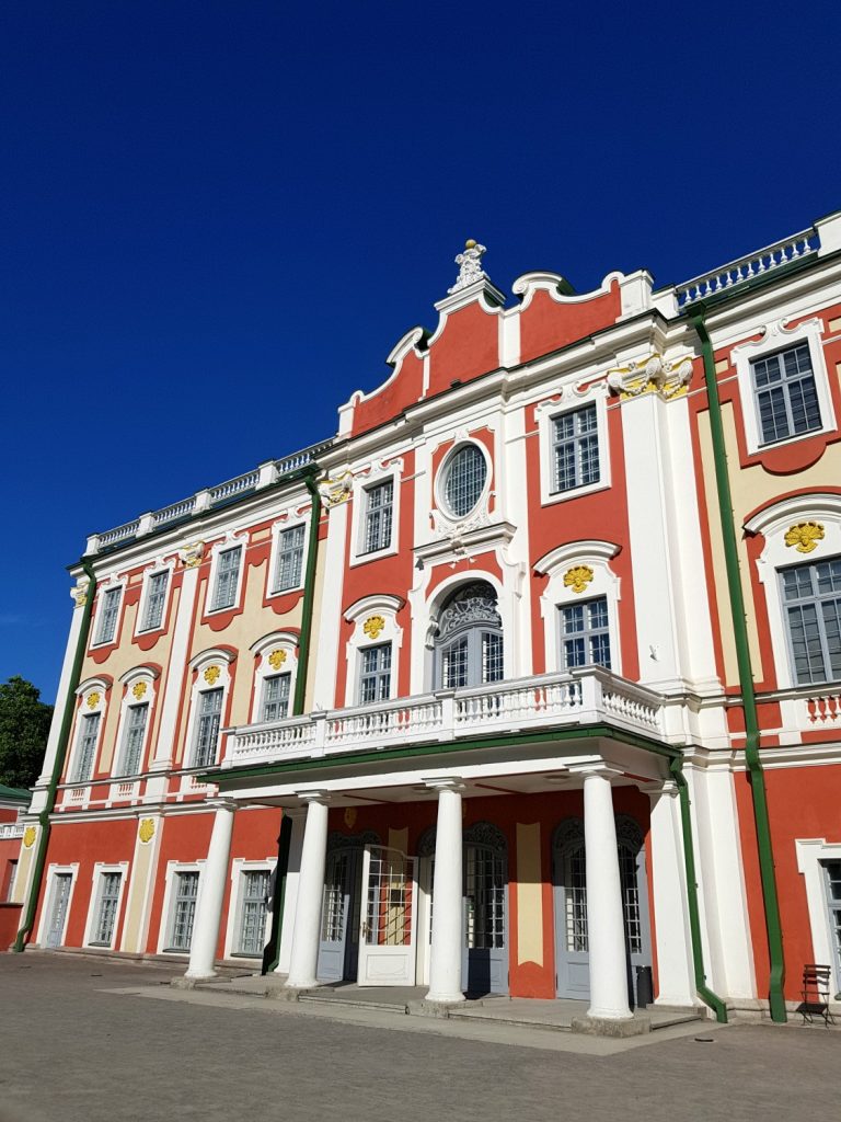 The bright red and white front of Kadriorg palace against a blue sky - the open green space is one of the many reasons to visit Tallinn, Estonia