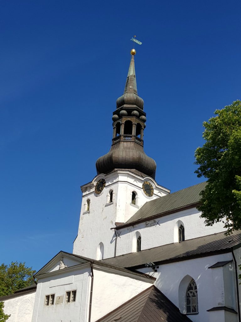 View to a black spire above a white church against a blue sky, in the city's Old Town - the city's famously fairytale architecture is just one of the many reasons to visit Tallinn, Estonia
