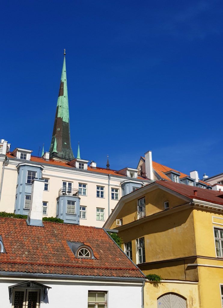 Bright buildings and a tall spire marked with green against a blue sky - the city's famously fairytale architecture is just one of the many reasons to visit Tallinn, Estonia