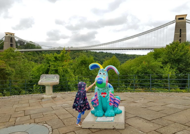 My daughter touches the Bristol Gromit statue, set on a viewpoint with the Clifton Suspension Bridge in the background - following the Gromit Unleashed 2 trail in Bristol, our review