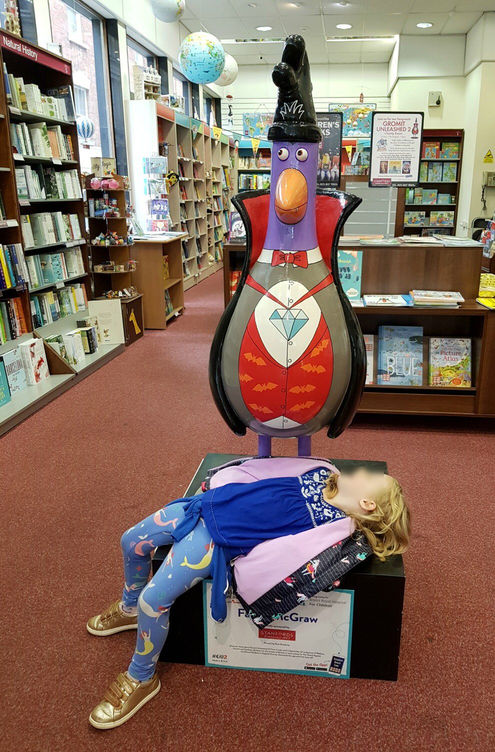 My daughter plays dead at the foot of a statue of Feathers McGraw dressed as a vampire in the Gromit Unleashed trail in Bristol