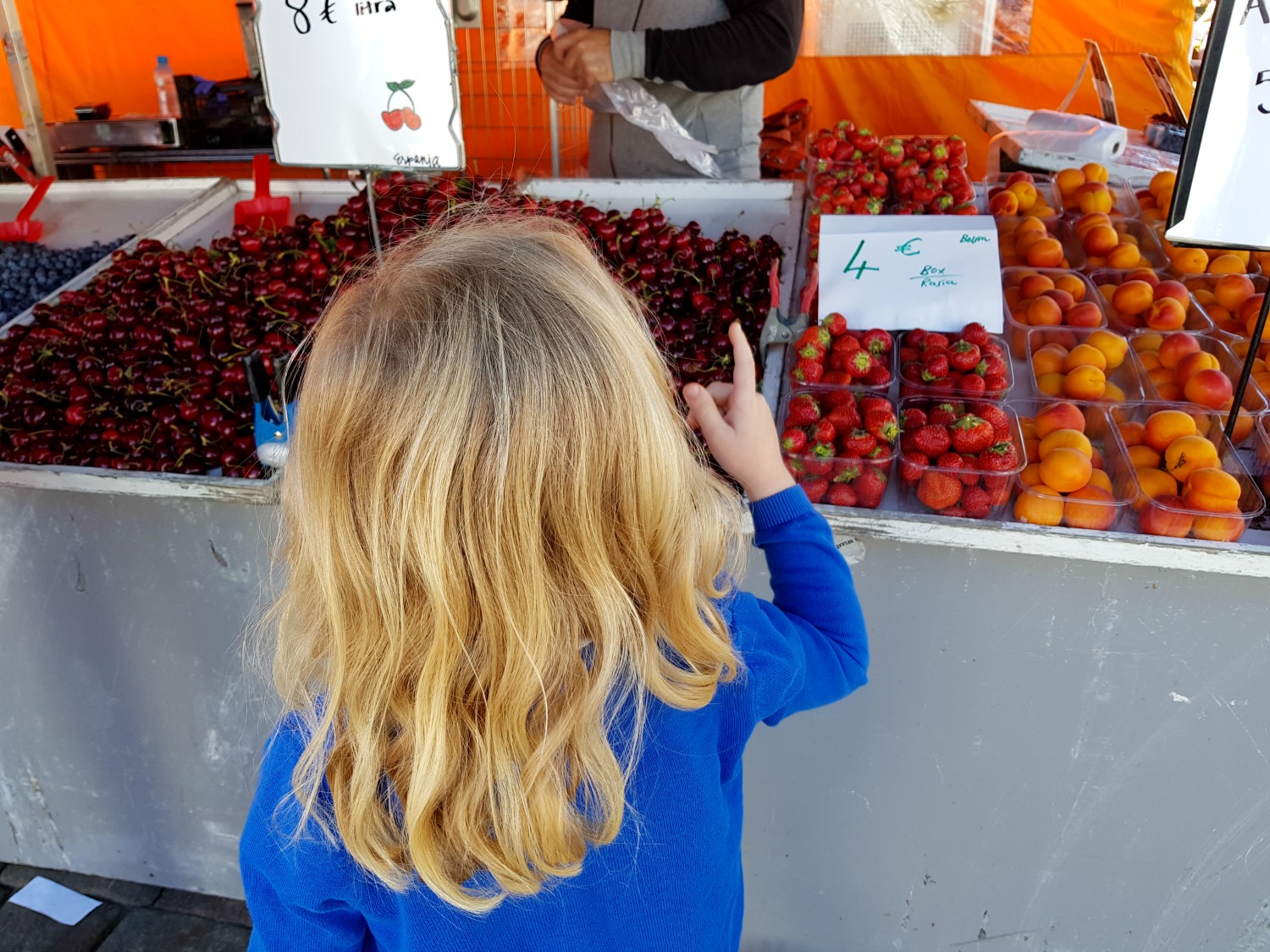 My daughter eyes up fruit at the market stall in Helsinki - the appreciation of the little things is one of the top answers to the question why visit Helsinki?