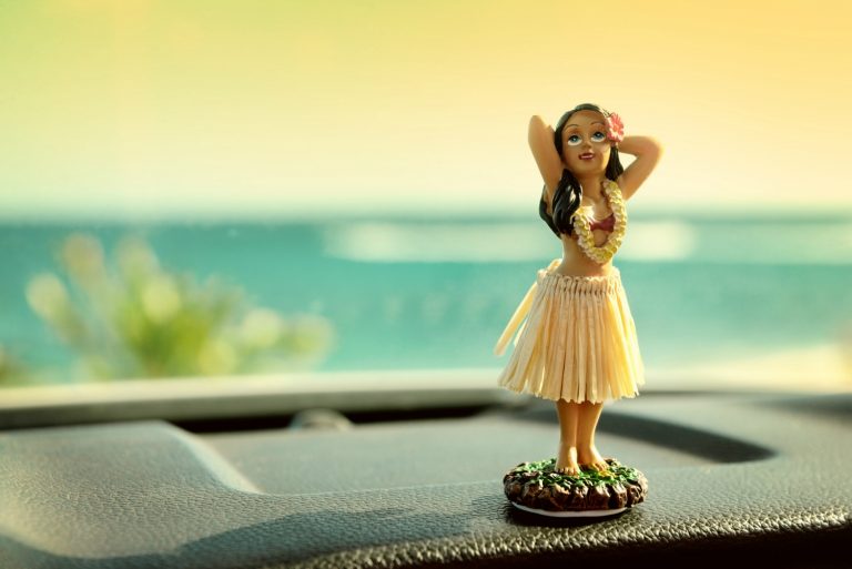 Hula dancer doll on the dashboard of a car with the ocean in the background - planning a dream Hawaii trip with kids