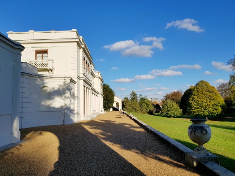 A view along the terrace to the rear of Gunnersbury House, the white building against a blue sky with the start of the lawns - my review of a free day out in London, visiting Gunnersbury Park Museum with kids