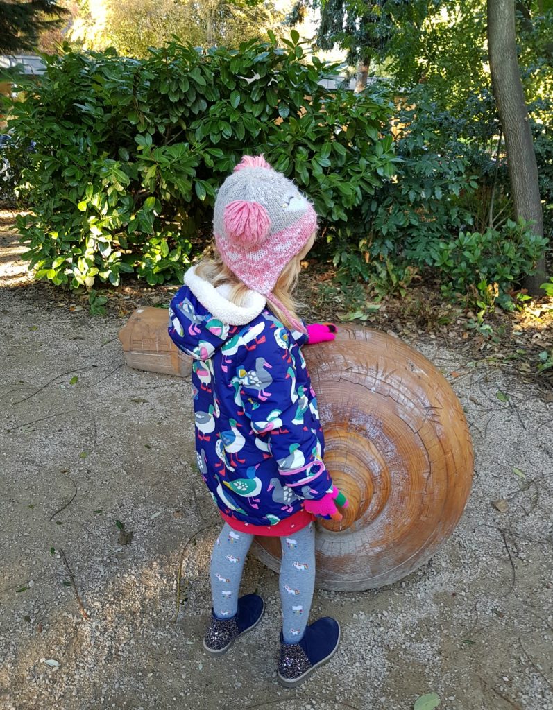 My daughter in winter hat and coat next to a carved wooden sculpture - my review of a free day out in London, visiting Gunnersbury Park Museum with kids