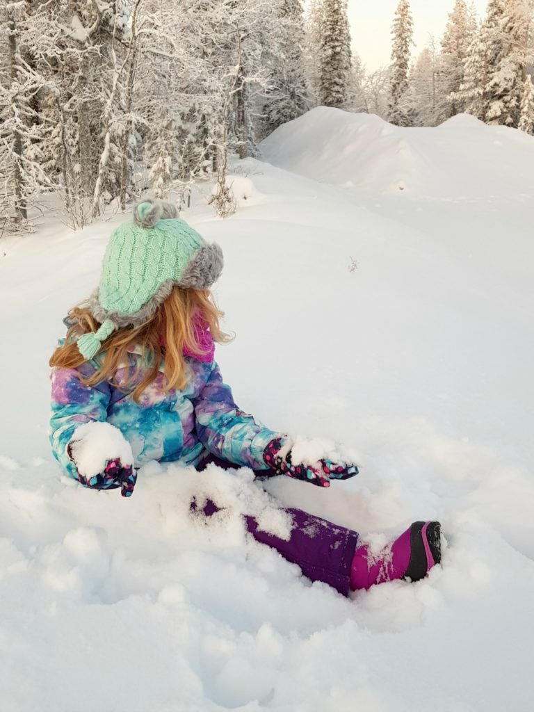 My daughter gets ready to throw snowballs while sitting in the snow in Lapland - my essential packing list for Lapland