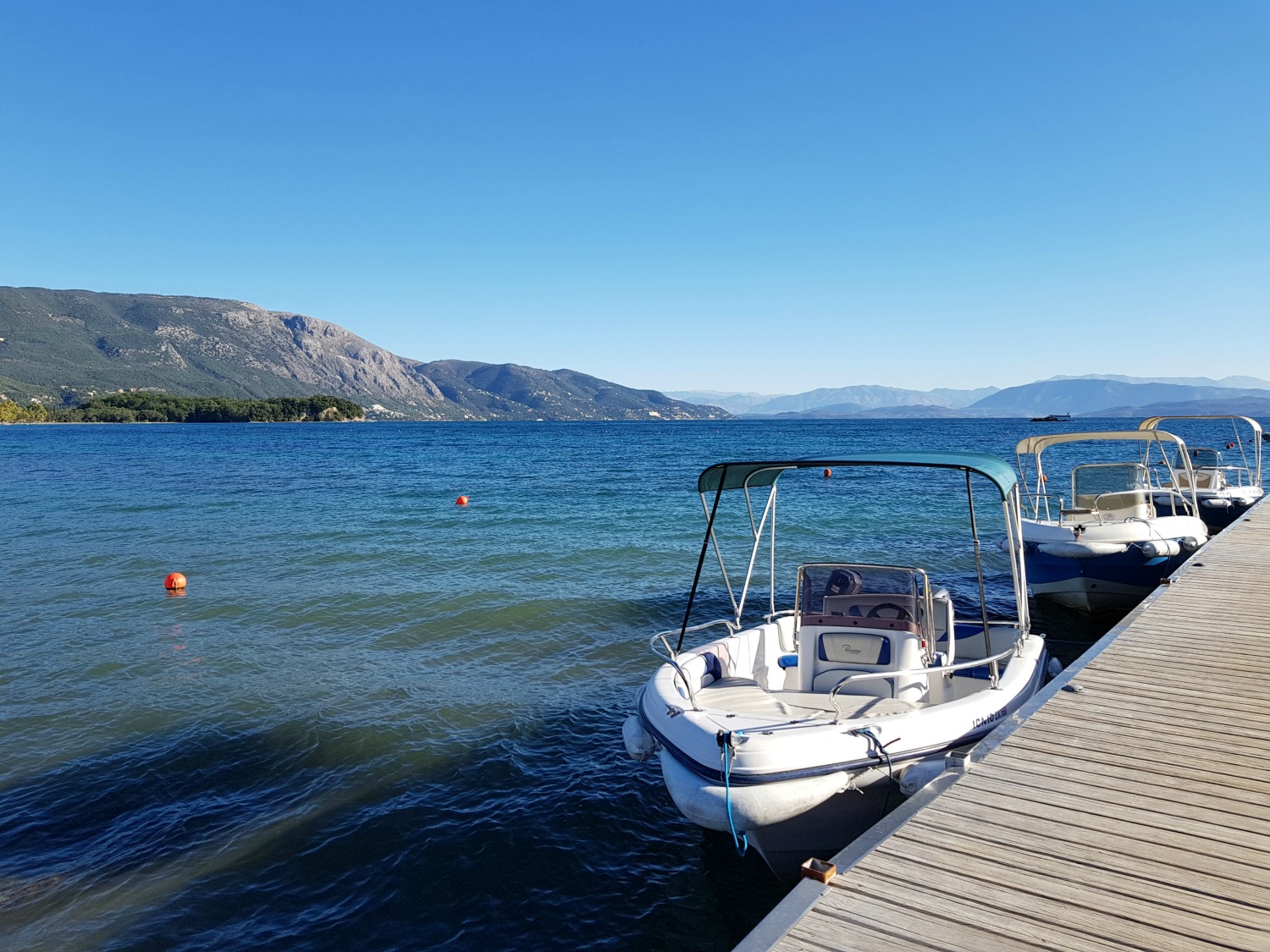 Boat docked just off the beachfront with the sea and hills behind at Ikos Dassia - my review of Ikos Dassia with kids, a family holiday in Corfu