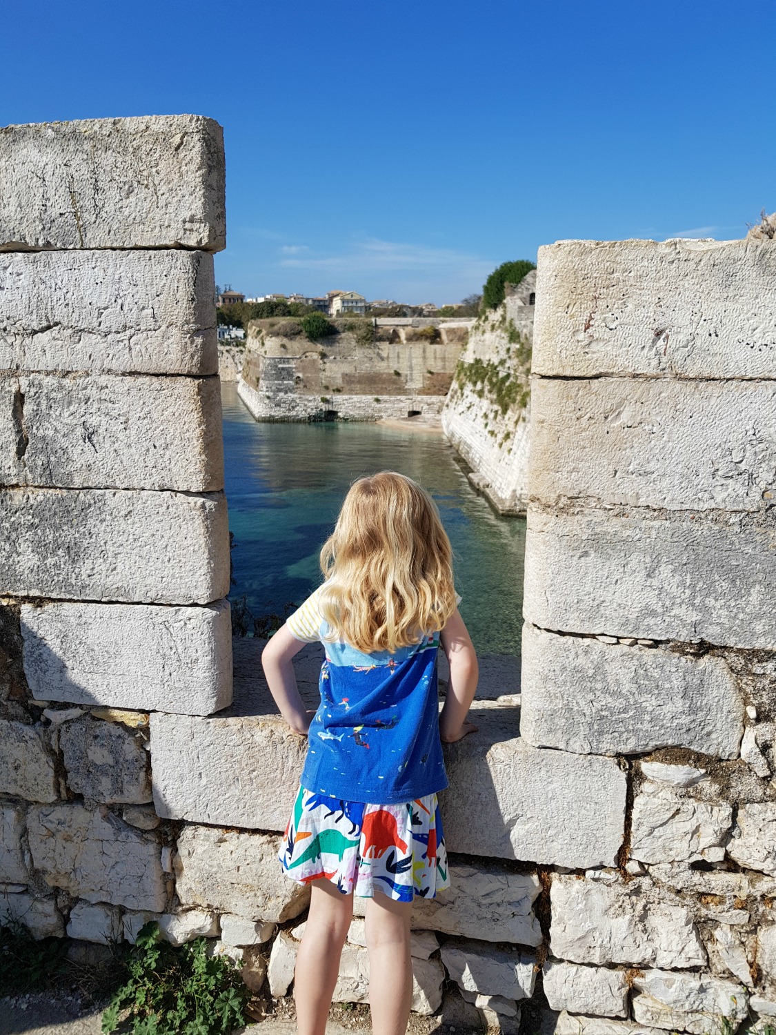 My daughter peers down onto the sea through fortifications at Corfu Town's old Venetian fortress - three things to do in Corfu Town with kids