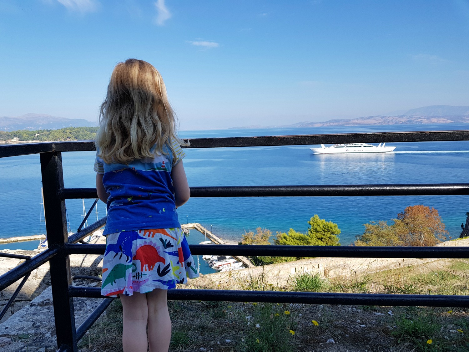 My daughter looks down onto the sea and a ferry from one of the viewpoints in Corfu Town's old Venetian fortress - three things to do in Corfu Town with kids