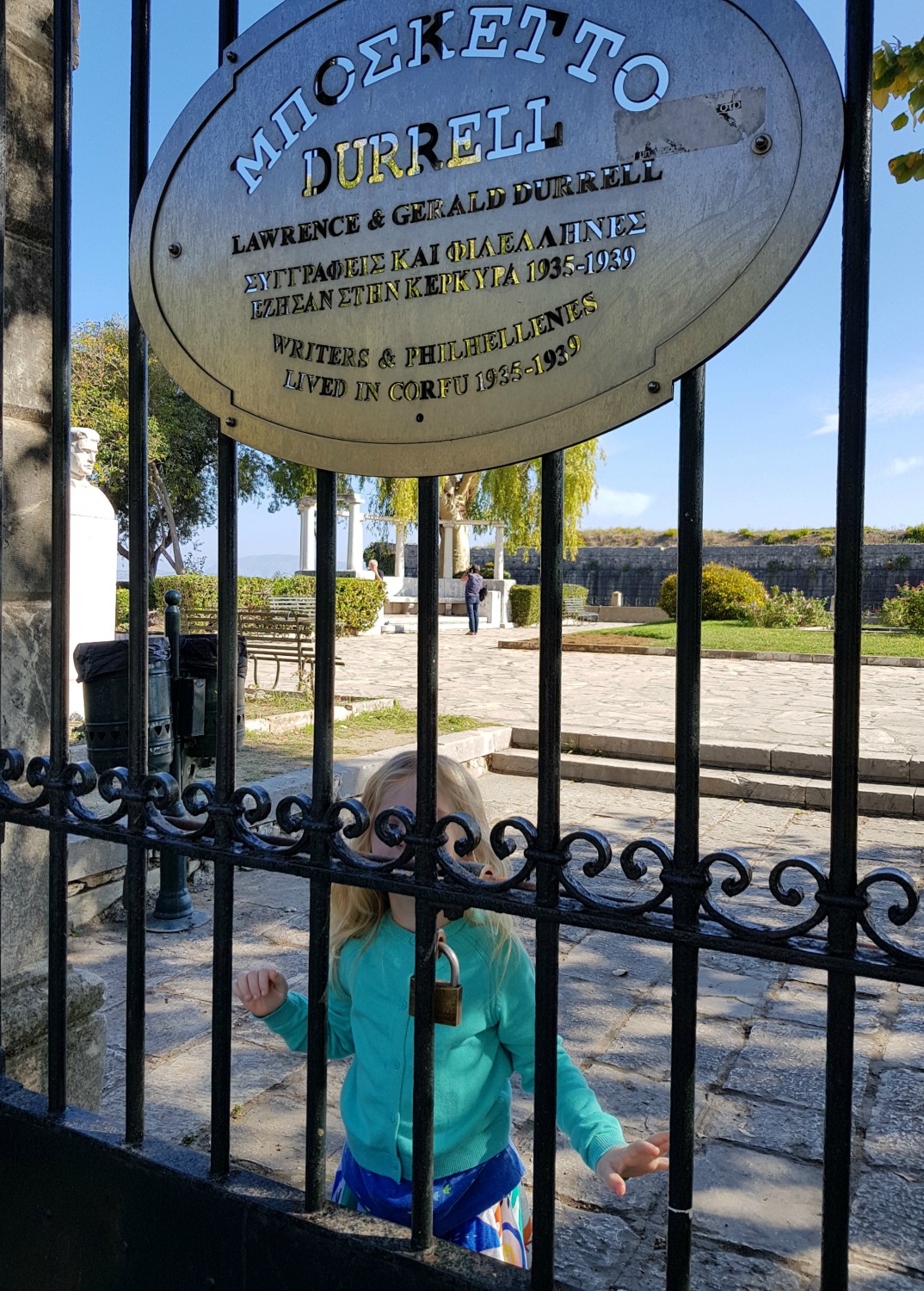 My daughter peers through wrought iron gates with a sign commemorating the Durrell family near Corfu Town's old Venetian fortress - three things to do in Corfu Town with kids