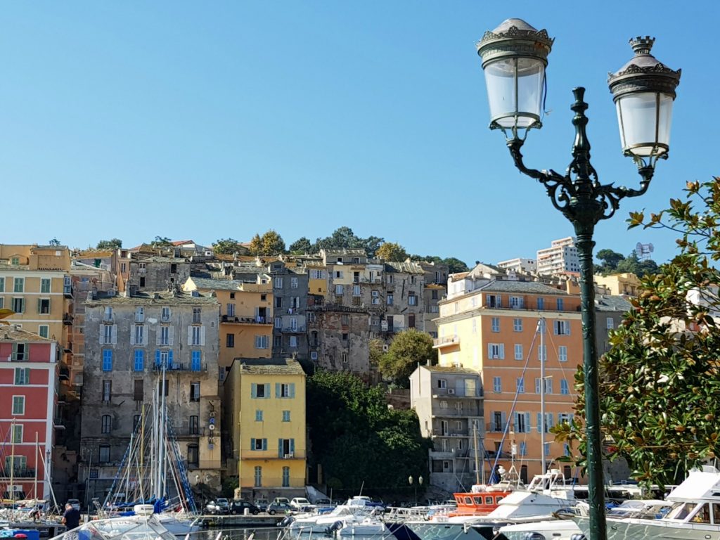 A view past a lampost across the old harbour to the pastel buildings of Bastia in Corsica - my Corsica short break visiting Bastia and Calvi in a long weekend