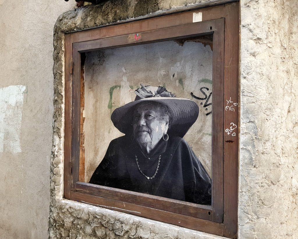 Black and white street art looking like a vintage photo of an old woman in a backstreet in Bastia, Corsica - my Corsica short break visiting Bastia and Calvi in a long weekend
