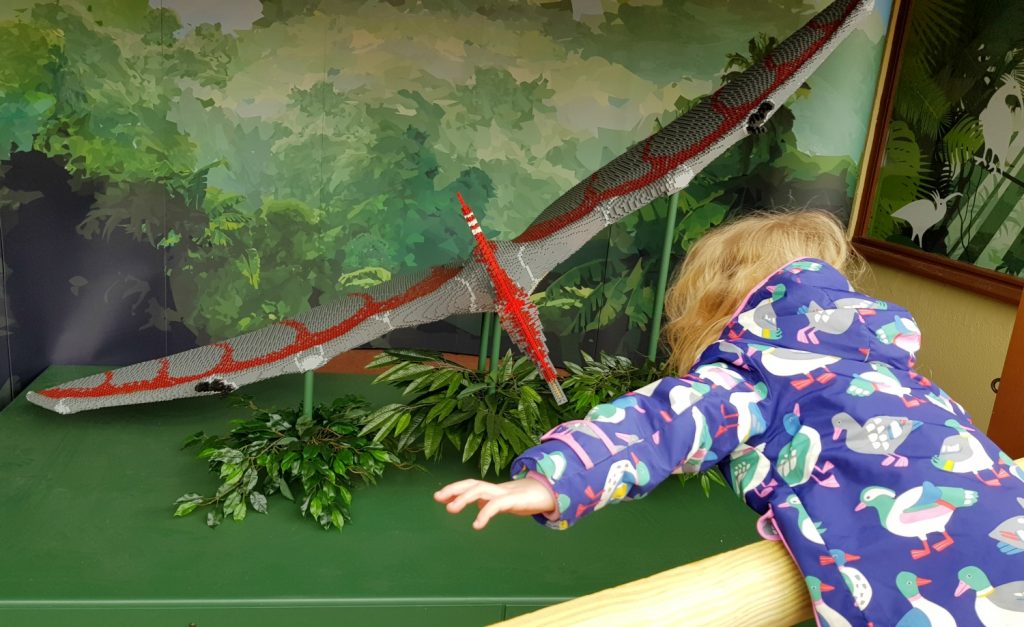 My daughter mimics a suspended red lego pteranodon, one of the Brickosaurs at Marwell Zoo