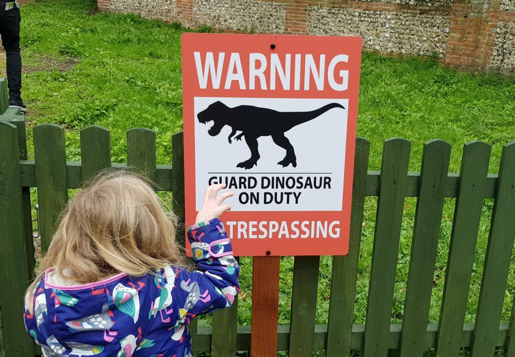 Girl pretends to be a dinosaur next to a warning sign on the Marwell Zoo Brickosaurs trail