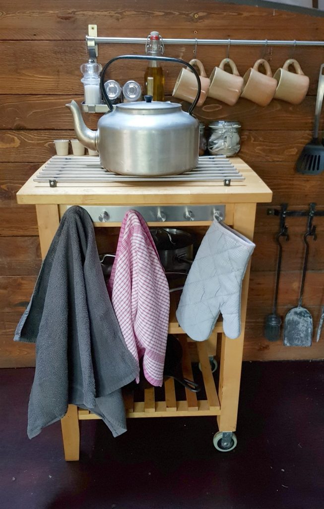 Small table with kettle and oven glove plus fire irons in the background - my Penhein glamping review