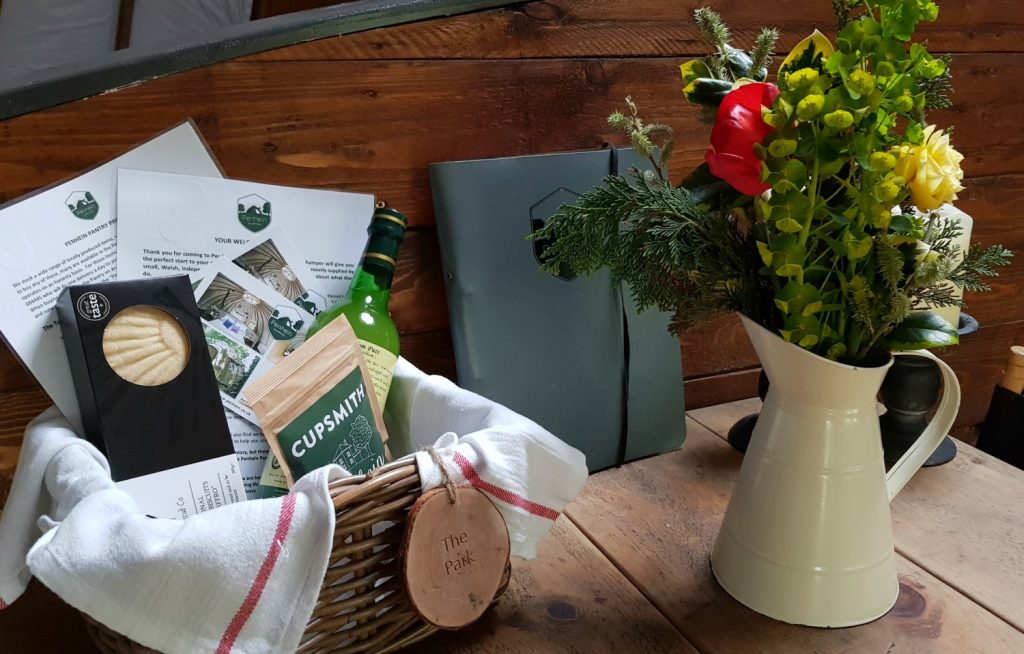 Welcome basket on the dining table next to flowers in a jug in our tent at Penhein glampsite
