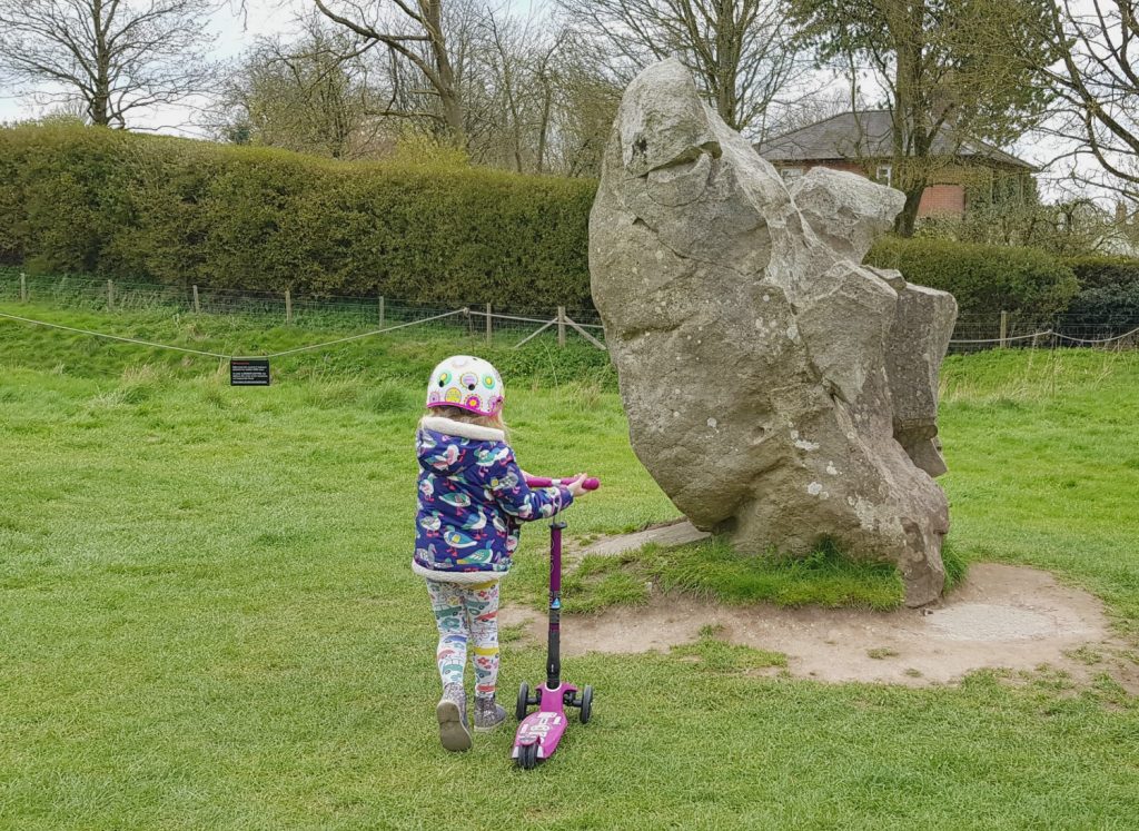 My daughter wheels her scooter over the grass to one of the standing stones at Avebury