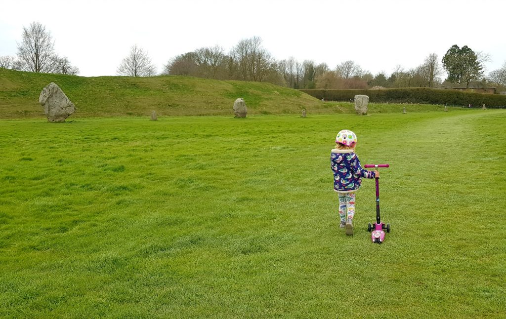 My daughter next to her scooter on the grass by the standing stones at Avebury, after testing how the three wheel scooter works on grass