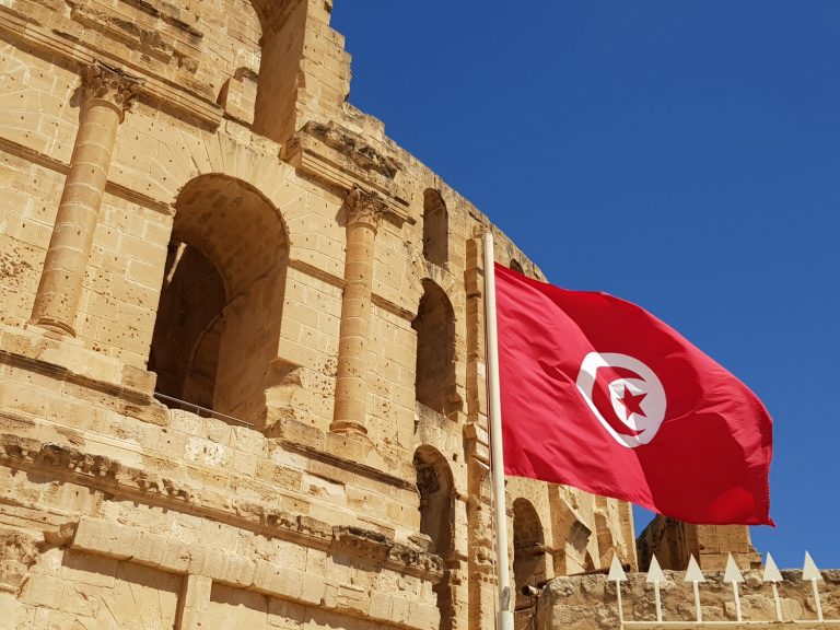 Red Tunisian flag flies in front of the Roman amphitheatre of El Jem - if you're asking yourself why visit Tunisia, I have seven reasons to explore Tunisia with kids