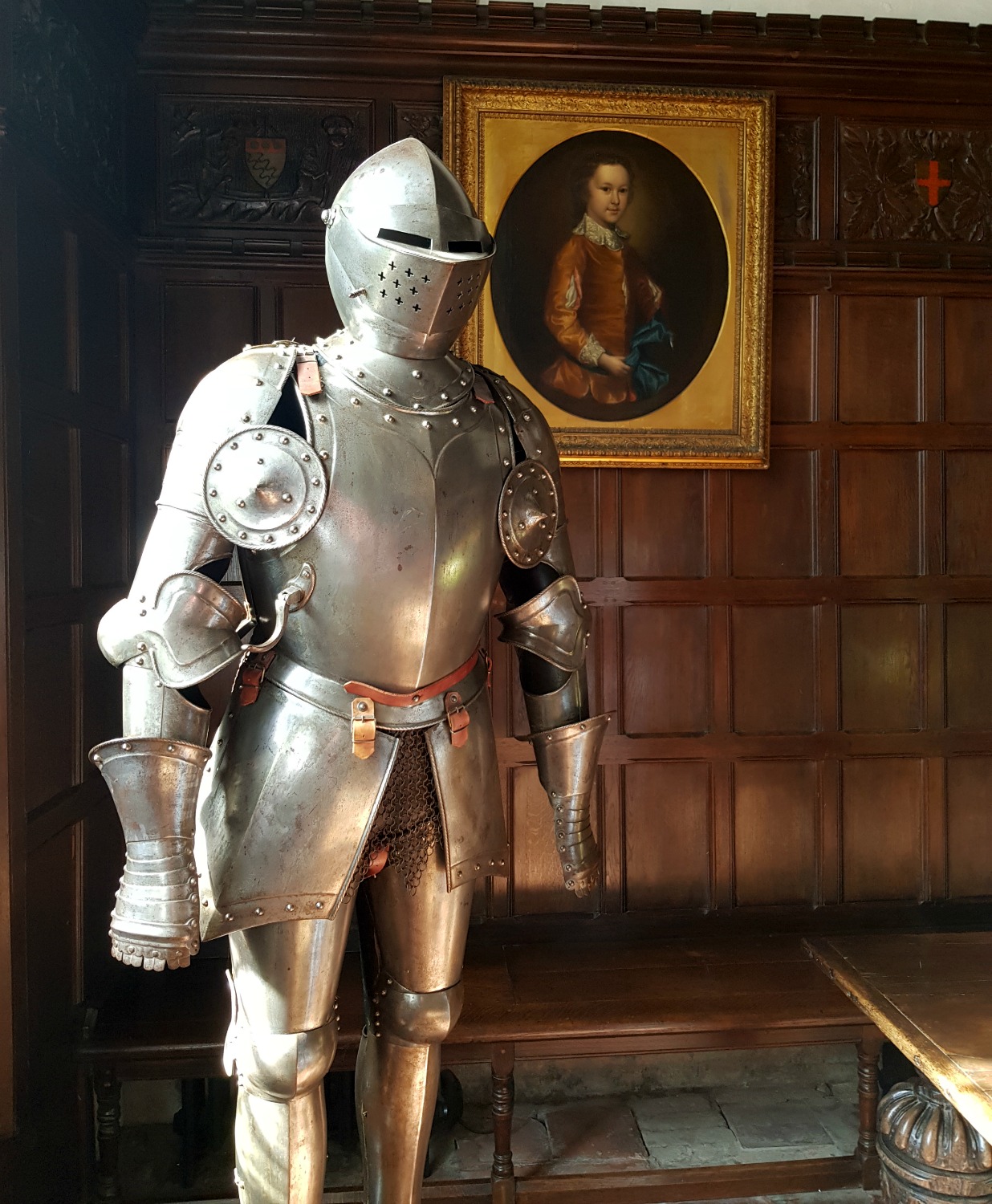Gleaming silver suit of armour with an old portrait behind in the Great Hall of Ightham Mote in Kent