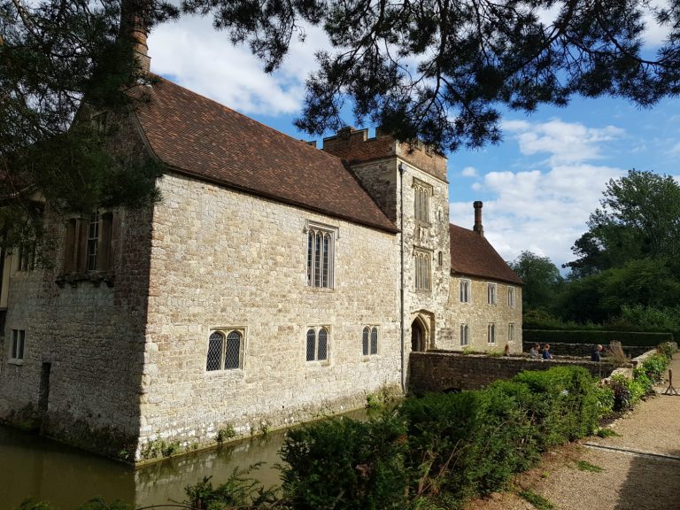 View of the side of Ightham Mote medieval manor house with its moat and a blue sky behind - visiting Ightham Mote with kids on a family day out in Kent