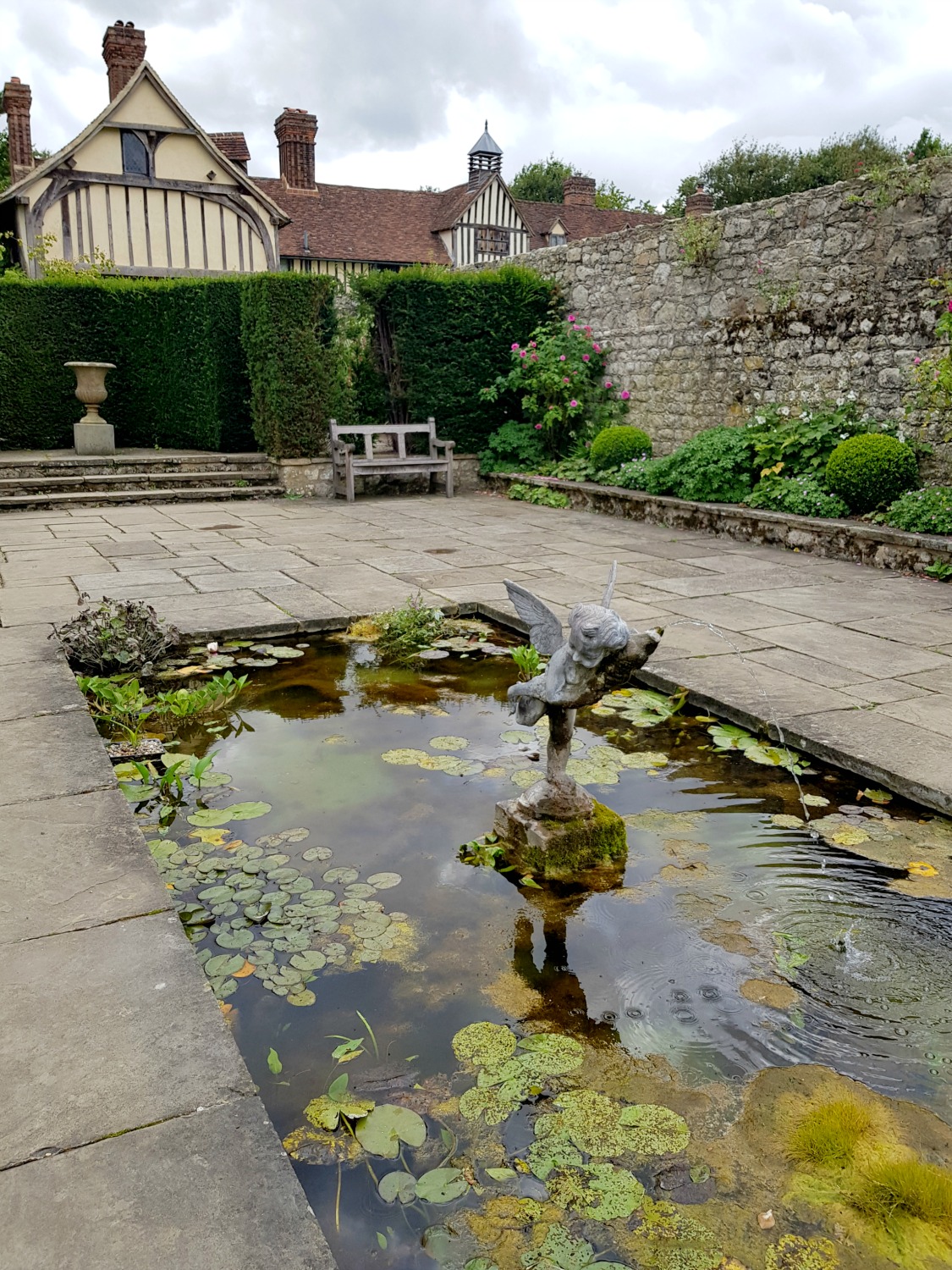View across the pool with statue in in the enclosed garden at Ightham Mote, the secret garden hidden at the back