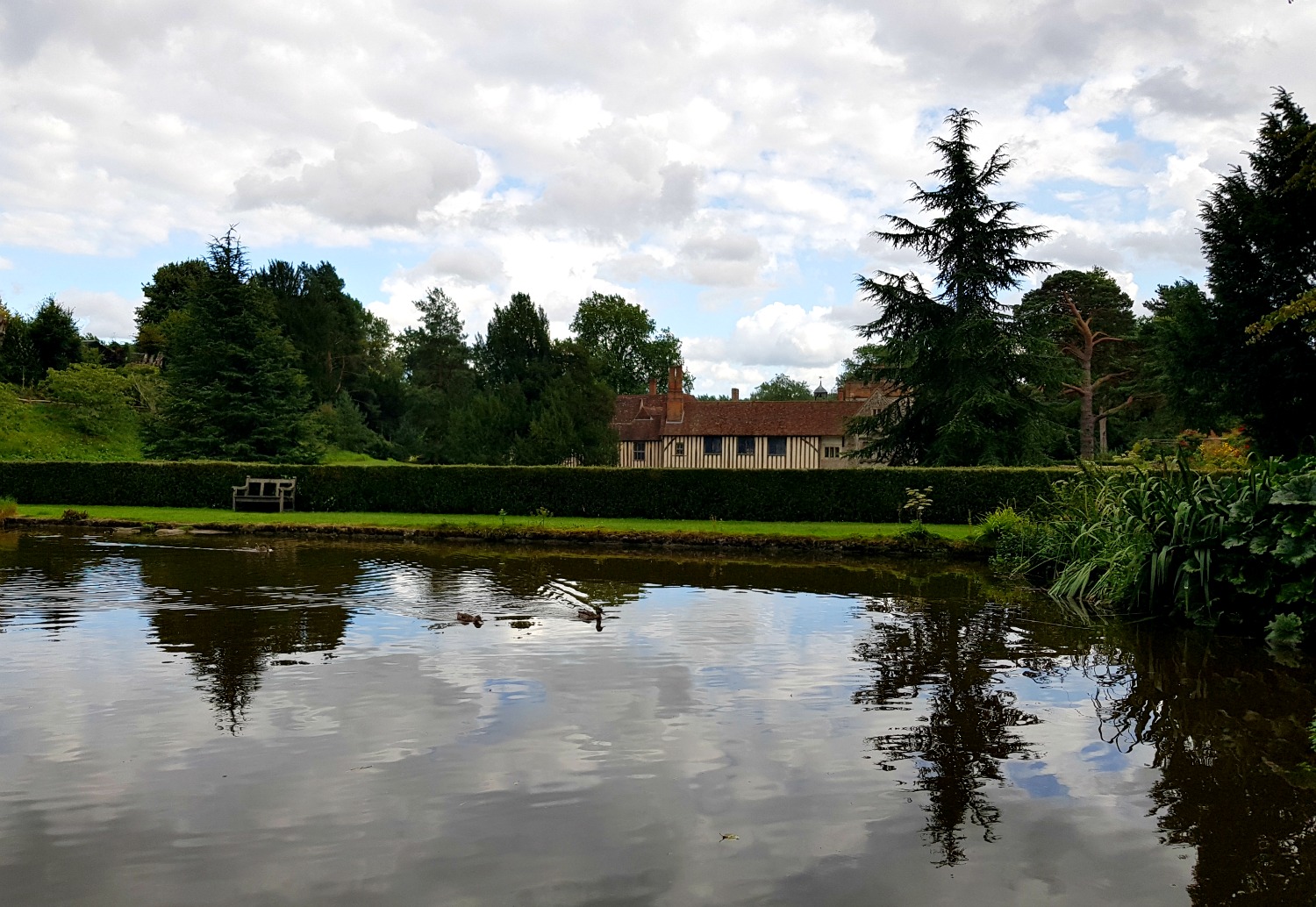 View of Ightham Mote across the lake, with the trees reflected in the water